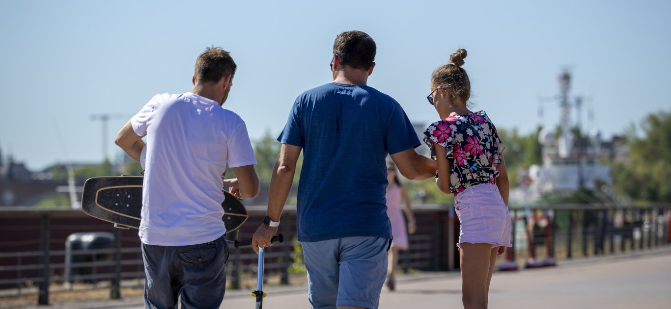 Trois promeneurs en skate et trottinette sur les quais rive gauche, sur la promenade des quais
