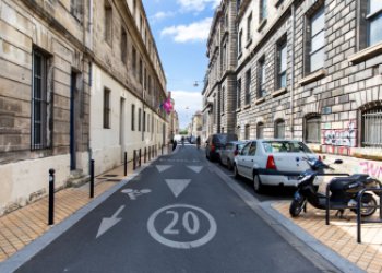 Vue d'une rue de Bordeaux avec des voitures et un scooter stationnés sur le côté droit 