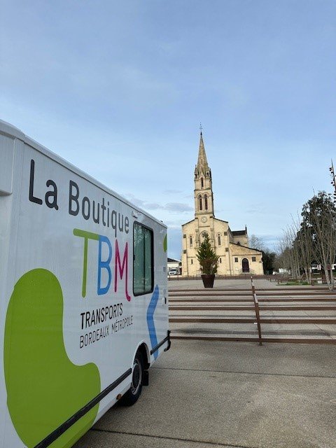 Au 1er plan la boutique mobile TBM stationnée sur une place ; au fond l'église de Gradignan